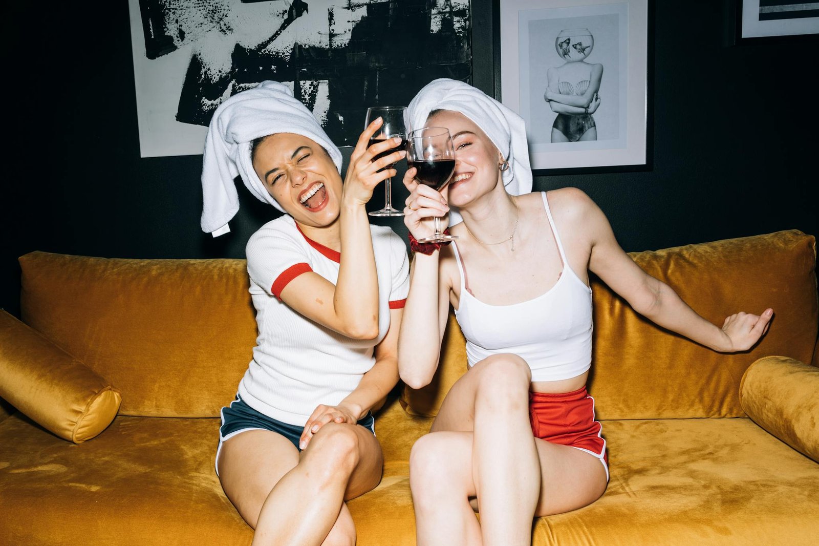 Two Young Women Sitting on a Yellow Sofa While Holding a Wine Glass With Red Wine